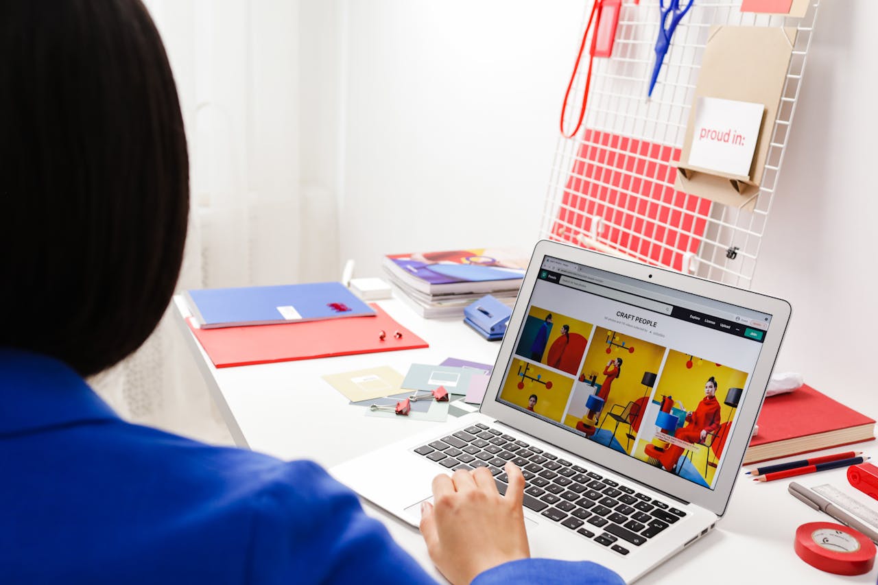 A woman in a blue jacket focused on a laptop screen in a colorful office workspace.